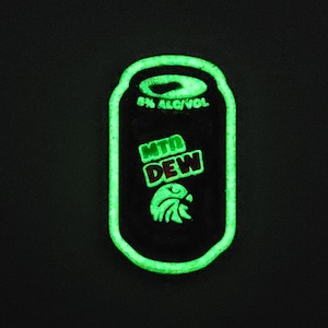 Op de afbeelding: Een groene glow-in-the-dark blikje met de woorden "MTN DEW" en "5% ALC/VOL" erop gedrukt.