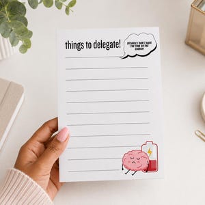May include: A white notepad with black horizontal lines, featuring the text "things to delegate!" and a speech bubble saying "BECAUSE I DON'T HAVE THE TIME OR THE ENERGY!" at the top, and a graphic of a sad pink brain leaning on a low battery icon.