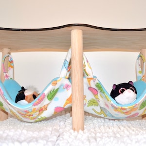 May include: Two hanging beds for small pets, made of wood and fabric. The beds are suspended from a wooden frame and have a blue and white floral pattern. Each bed has a plush toy inside.