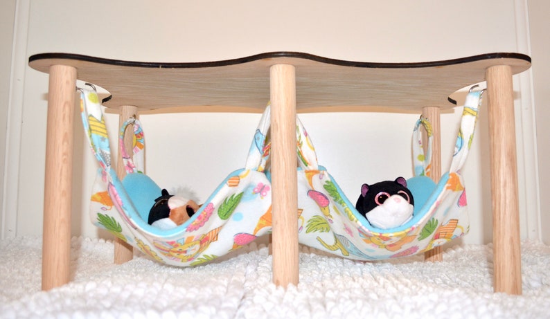 May include: Two hanging beds for small pets, made of wood and fabric. The beds are suspended from a wooden frame and have a blue and white floral pattern. Each bed has a plush toy inside.