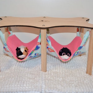 May include: A wooden platform with two pink and blue fabric hammocks hanging from it. The hammocks are filled with stuffed animals.