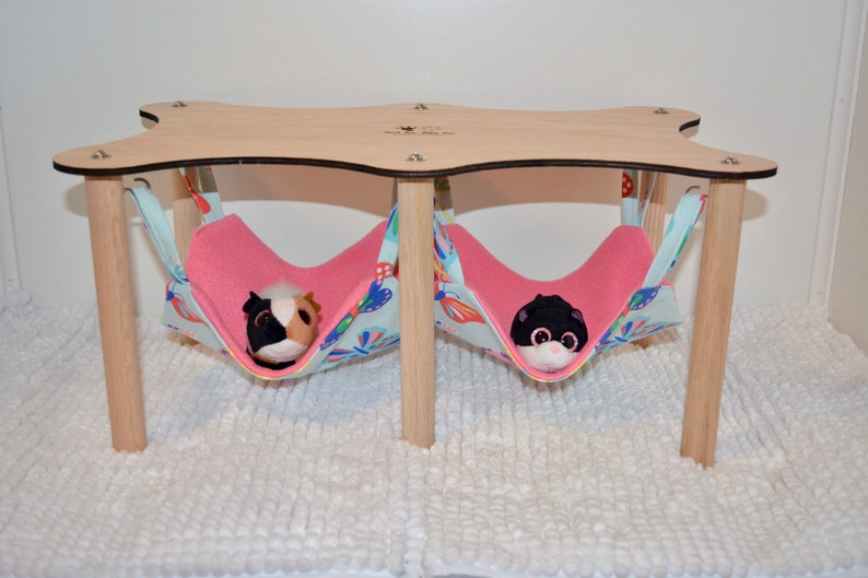 May include: A wooden platform with two pink and blue fabric hammocks hanging from it. The hammocks are filled with stuffed animals.