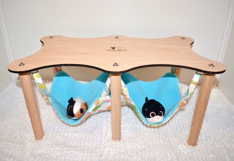 May include: A wooden platform with two blue fabric hammocks hanging underneath. The platform has a rounded, star-shaped top with the text "Small Pet Mini Fun" engraved on it. Two small plush toys are inside the hammocks.