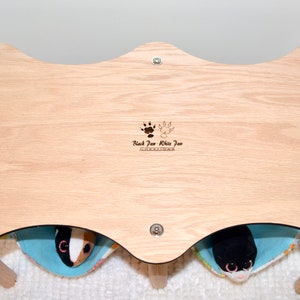 May include: A wooden pet bed with two separate compartments, each with a soft blue and white fabric lining. The bed is made by "Black Paw White Paw Creations".