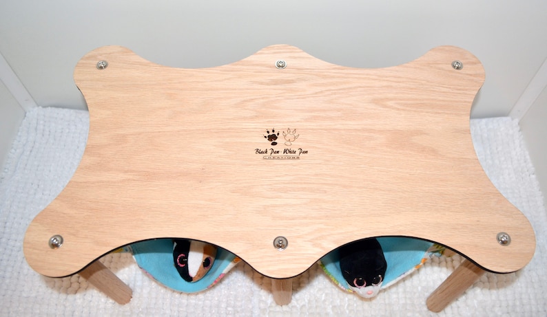 May include: A wooden pet bed with two separate compartments, each with a soft blue and white fabric lining. The bed is made by "Black Paw White Paw Creations".