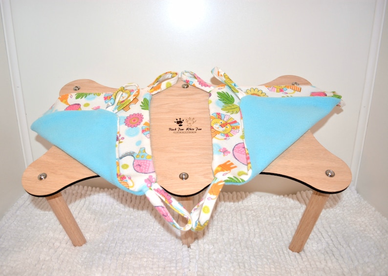 May include: A light blue and white fabric cat hammock with a colorful animal print. The hammock is attached to a wooden stand with four legs.