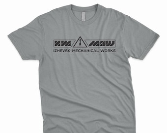 May include: A heather grey t-shirt with a black graphic of a warning sign with the text "IZHEVSK MECHANICAL WORKS" underneath.