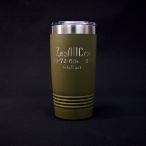 May include: Olive green travel tumbler with a silver rim and lid. The tumbler features etched text including "7,62/ПС гж", "09-72-60", and "440 шт". The bottom has three horizontal grooves. The tumbler is designed to keep drinks hot or cold.