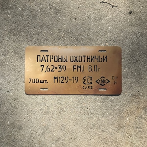 May include: A gold-colored metal tag with black text that reads "Патроны охотничьи 7,62×39 FMJ 8,0г 700шт. M129-19 CE CA03 СГИС"