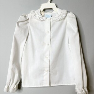 May include: White long-sleeve blouse with a lace collar and cuffs. The blouse has a button-up front and a slightly puffed sleeve.
