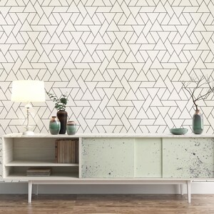 May include: A white cabinet with two doors and three shelves. The cabinet has a light wood finish and is decorated with a geometric pattern. The cabinet is sitting on a wooden floor. There is a lamp, a vase with branches, and two other vases on top of the cabinet.