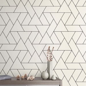 May include: A white wall with a black geometric pattern of overlapping triangles. A wooden table with a clock, a book, and decorative items sits in front of the wall.