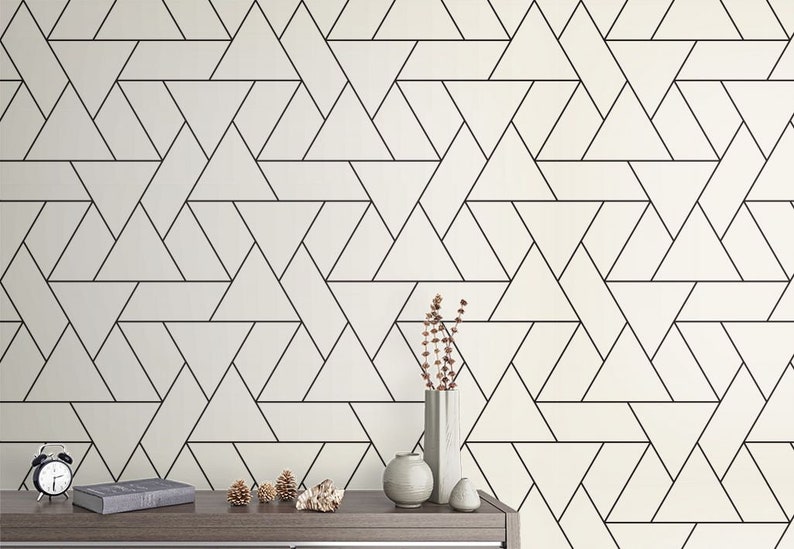 May include: A white wall with a black geometric pattern of overlapping triangles. A wooden table with a clock, a book, and decorative items sits in front of the wall.