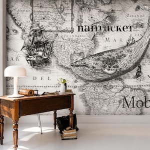 May include: A wall mural featuring a vintage-style black and white map background with a large whale illustration, a sailing ship, and the text "nantucket" and "Moby" printed across the surface, displayed behind a wooden desk and lamp.