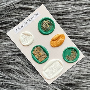 May include: Six wax seals on a white card with the text "A Study in Drowning". The seals are in various designs and colours, including green, gold, and white.