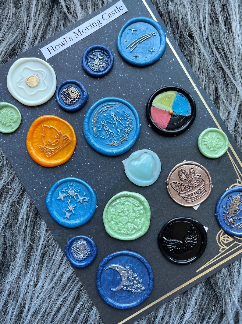 May include: A collection of colorful wax seals with various designs, including stars, moons, and floral patterns. The seals are arranged on a dark background, with the text "Howl's Moving Castle" visible at the top.