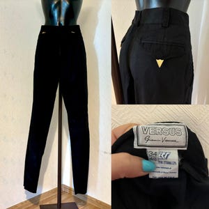May include: Black pants with a gold zipper detail and a Versus Gianni Versace label. The label has the text "Versus Gianni Versace" and the size "34 48".