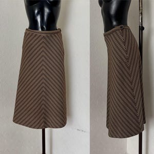 Puede incluir: Falda a rayas marrón y beige con un diseño de chevron. La falda se muestra en un maniquí y presenta una cintura ajustada y un dobladillo acampanado. La falda está hecha de una tela tejida.