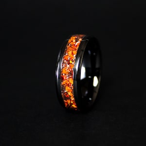 May include: A black tungsten carbide ring with a band of orange and brown glitter embedded in the metal.