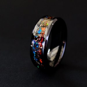 May include: A black tungsten carbide ring with a colorful inlay of opal. The inlay is a band of red, orange, yellow, and blue.