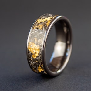 May include: A black ring with a band of gold flakes embedded in the surface.