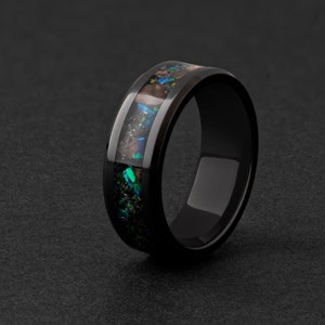 Könnte beinhalten: Ein schwarzer Keramikring mit einer Einfassung aus irisierendem grün-braunem Opal.