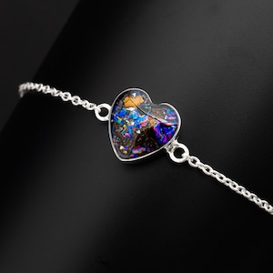 May include: A silver chain bracelet with a heart-shaped pendant. The pendant is filled with iridescent blue, purple, and gold glitter.