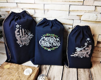 May include: Three navy blue drawstring bags with embroidered Christmas designs. One bag features candles and pine needles, another says "MERRY CHRISTMAS" with a wreath, and the third has a bird on a branch.
