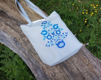 May include: A gray linen tote bag with blue and turquoise embroidered flowers. The bag has two long straps.
