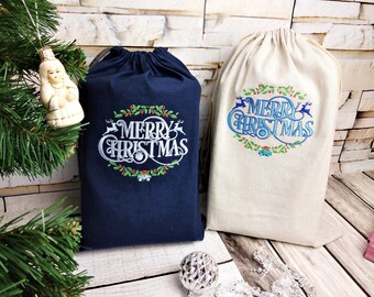 May include: Two Christmas gift bags. One is navy blue, the other is beige. Both bags have a drawstring closure and embroidered text that reads "MERRY CHRISTMAS" in white and blue, surrounded by festive designs.