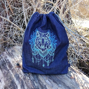 Könnte beinhalten: Eine blaue Jeans-Kordeltasche mit einem weißen Wolf-Mandala-Design, das auf der Vorderseite gestickt ist. Die Augen des Wolfes sind blau und das Design enthält Federn und Perlen.