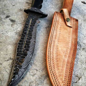 May include: A black and silver patterned knife with a black handle and a brown leather sheath.