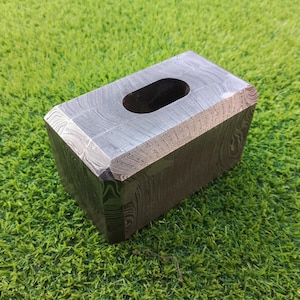 May include: A rectangular, silver-coloured hammer with a textured surface and a round hole in the top. The hammer is made of Damascus steel and has a unique, swirling pattern.