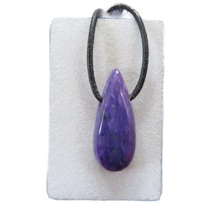 Könnte beinhalten: Ein tropfenförmiger, violetter Anhänger mit einer schwarzen Kordel. Der Anhänger hat eine tiefviolette Farbe mit helleren Streifen und Mustern. Die Kordel ist oben geschlungen, was darauf hindeutet, dass es sich um eine Halskette handelt.