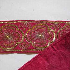 Könnte beinhalten: Ein rosa Stoffbesatz mit goldenen Pailletten und Stickereien in einem Blumenmuster.