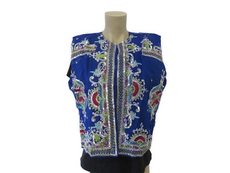 May include: A sleeveless blue vest with intricate silver and colorful embroidery. The vest has a high neckline and a button closure.