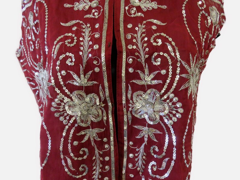 May include: A red sleeveless vest with silver sequins and embroidery in a floral pattern.