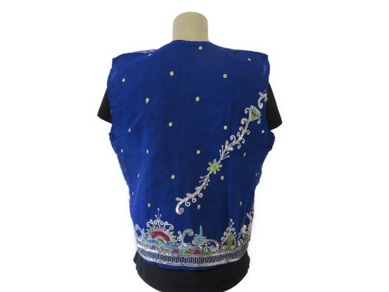 May include: A blue sleeveless vest with silver and colorful embroidery. The vest has a floral design and is decorated with small white dots.