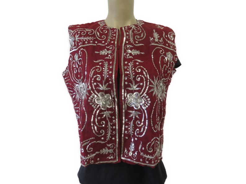 May include: A sleeveless vest with a burgundy base and silver embroidery. The embroidery features floral patterns and swirls.