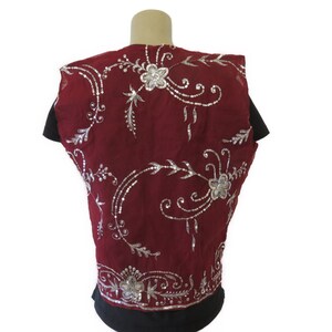 May include: A sleeveless burgundy vest with silver embroidery featuring floral designs. The vest is made of a sheer fabric and has a delicate, feminine look.