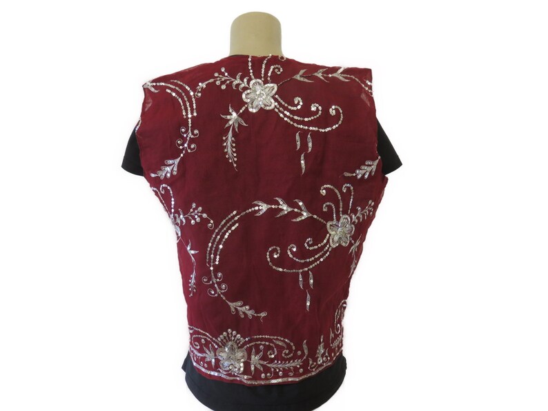 May include: A sleeveless burgundy vest with silver embroidery featuring floral designs. The vest is made of a sheer fabric and has a delicate, feminine look.
