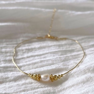 May include: A delicate gold chain anklet with a single white pearl and gold bead accents.