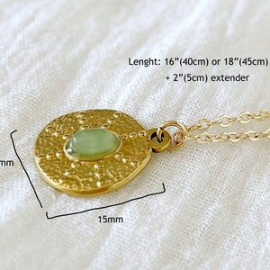 Gold necklace with a round pendant featuring a green gemstone. The pendant is 1.5 inches in diameter and has a textured surface. The necklace is 16 inches long with a 2-inch extender.