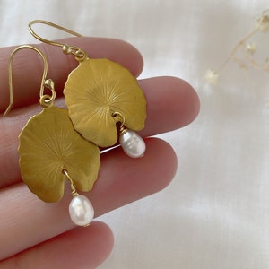 Gold leaf earrings with a pearl dangle. The earrings are shaped like a water lily leaf with a textured surface. The pearl is white and slightly round.