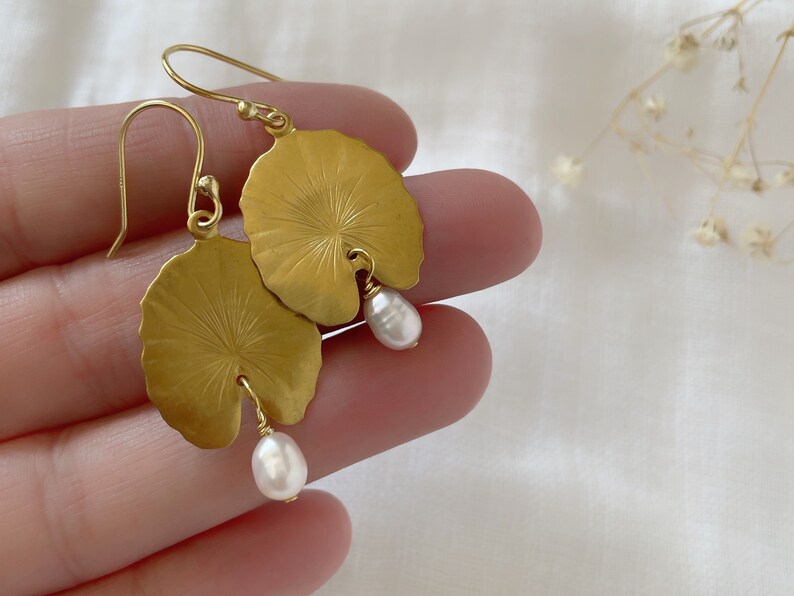 Gold leaf earrings with a pearl dangle. The earrings are shaped like a water lily leaf with a textured surface. The pearl is white and slightly round.