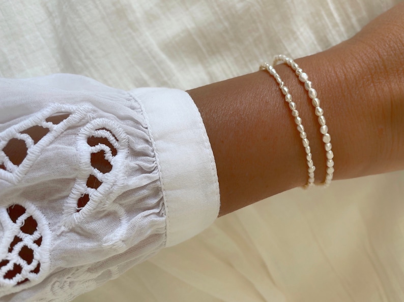 May include: Two silver beaded bracelets stacked on a wrist. The bracelets are made of small, round beads.