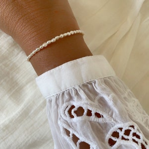 May include: A delicate bracelet made of small, white pearls. The bracelet is on a person's wrist.