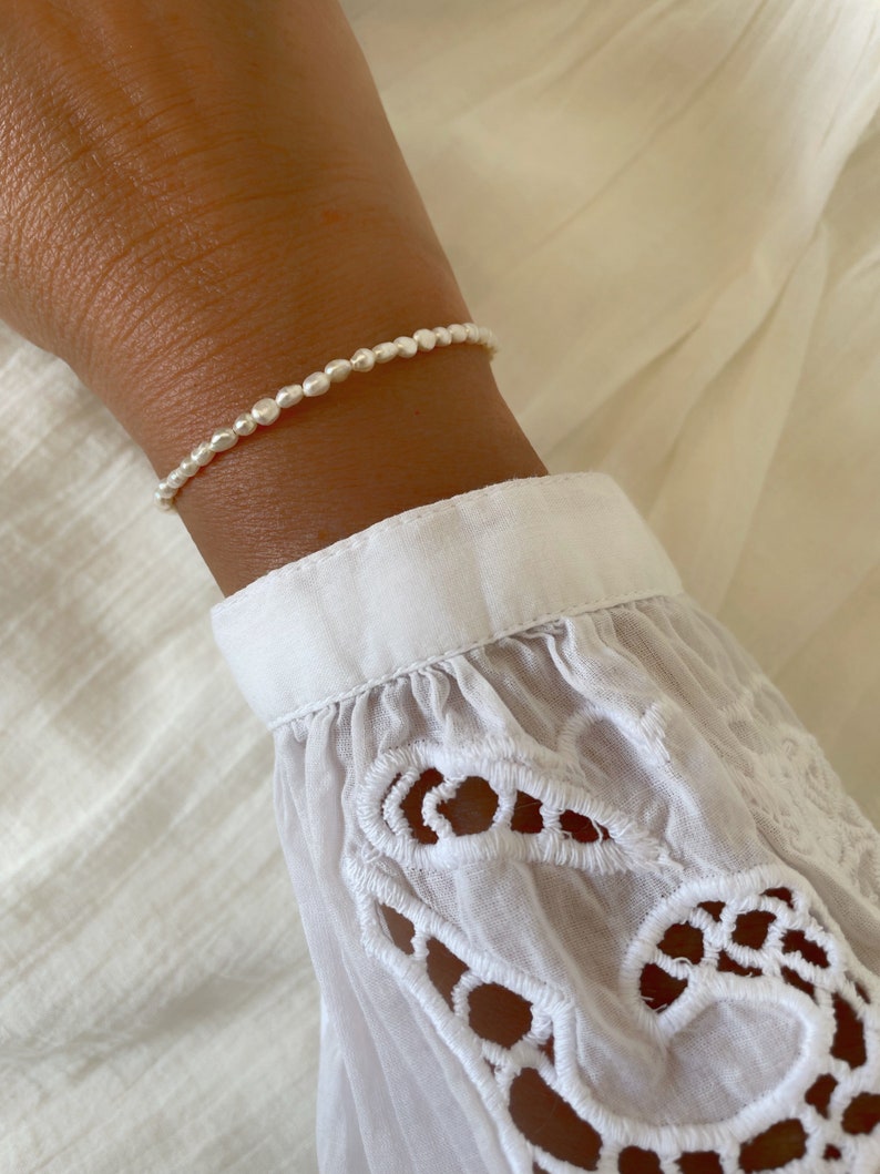 May include: A delicate bracelet made of small, white pearls. The bracelet is on a person's wrist.