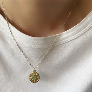 A dainty gold chain necklace with a round pendant featuring an oval shaped green gemstone.