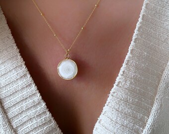 May include: A gold chain necklace with a white agate pendant. The pendant is round and has a delicate gold rim.